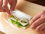 (1)のパンにバターまたはマヨネーズを塗り、それぞれの具材をのせてパンの端からクルクルと巻き、ラップで包む。