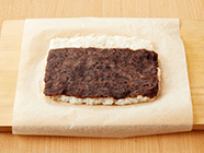 クッキングシートに(2)を幅20cm、奥行き15cm程度に広げ、奥側を3cm程残してあんこを広げ、巻き寿司の要領で手前から巻いていく。